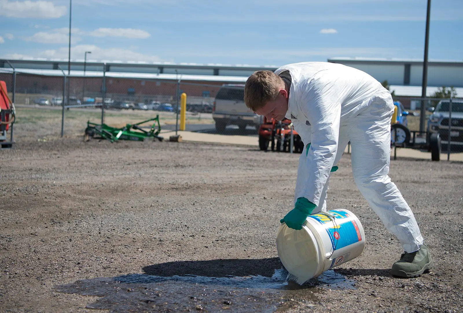Technicien en combinaison blanche versant un produit à l’extérieur